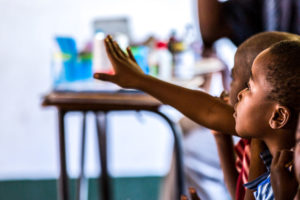 child raises hand in African classroom in Zimbabwe